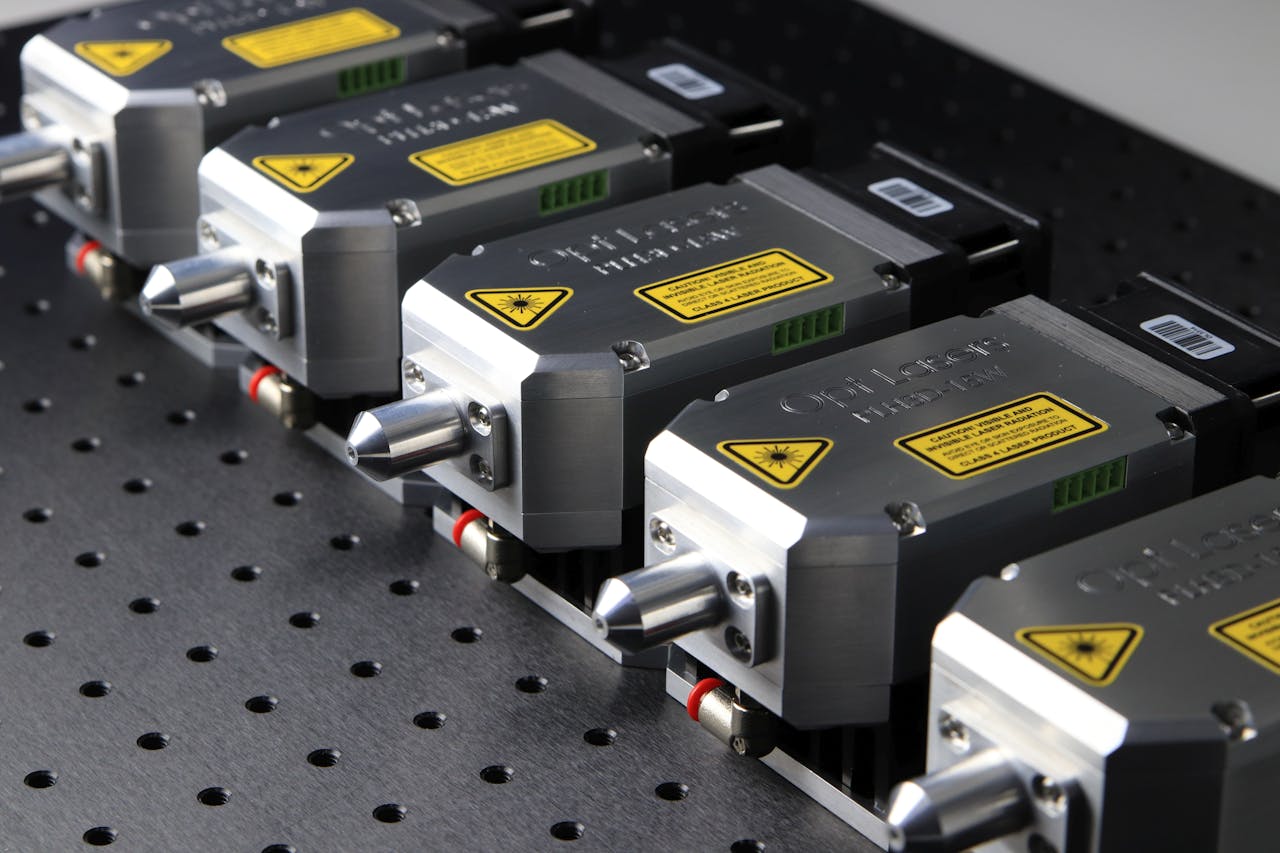 services-02 Detailed close-up of industrial laser modules with warning labels on a perforated metal surface.