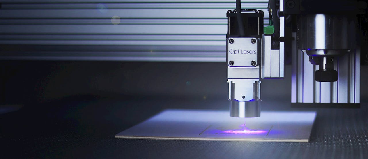gallery-6 Close-up of a laser engraver working on a surface under blue lighting.