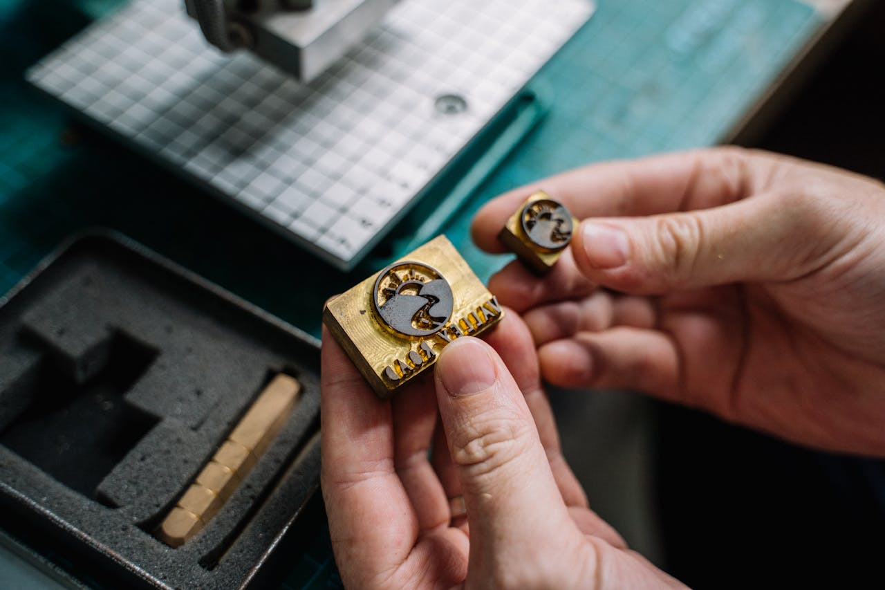 about-01 Close-up view of hands holding handcrafted brass stamps on a workbench.